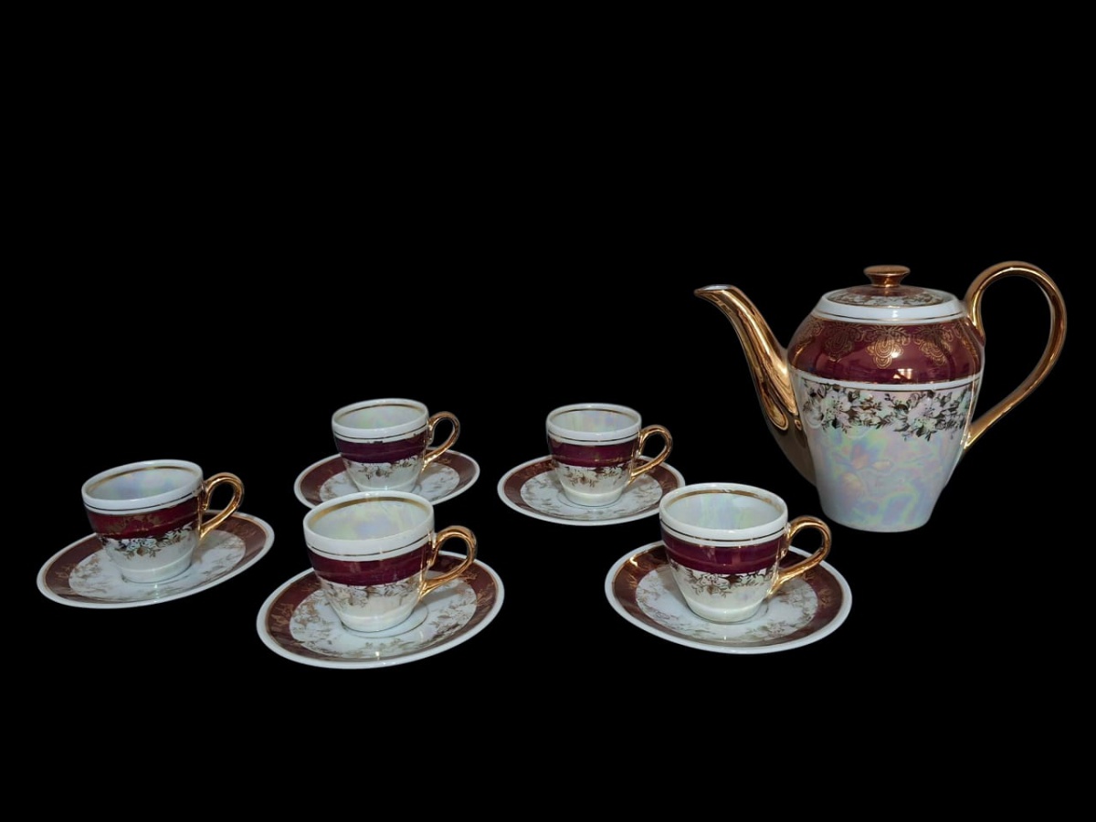 Belo jogo de café em porcelana, decorada em cores vinho e dourada, contando com cinco xícaras com pires e um bule.