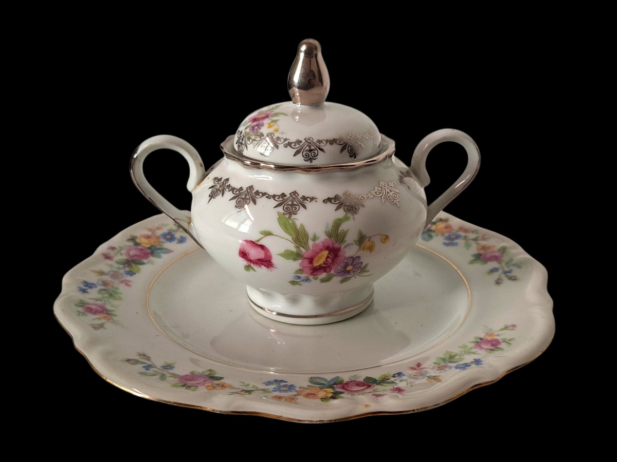 Bela dupla com açucareiro em porcelana brasileira e pratinho em porcelana polonesa, ambos com decoração muito similar. 10cmx20cm.