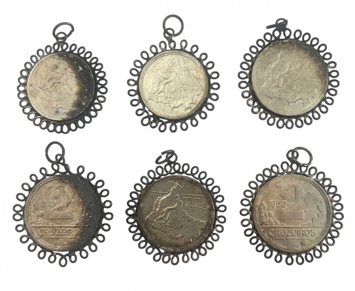 Conjunto com 6 pingentes antigos, confeccionados a partir de moedas brasileiras de 1 e 2 Cruzeiros (décadas de 19401950), montadas em aros metálicos trabalhados, típicos de uso popular e religioso. Peças com pátina ...