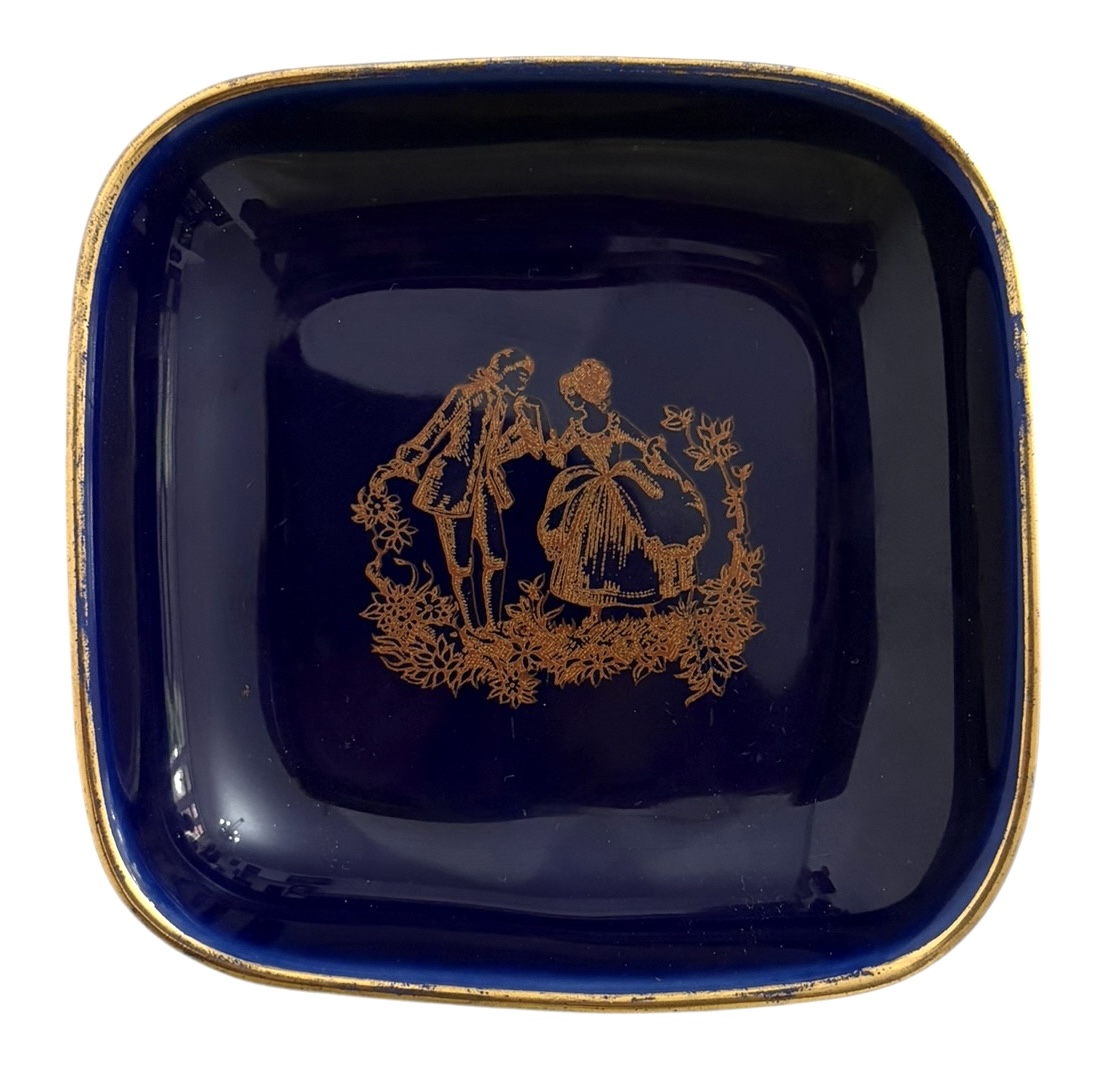 Porta alianças em pasta de porcelana francesa LIMOGES  Castel. Peça esmaltada em azul cobalto, formato quadrado, rica decoração dourada central com cena galante em estilo rococó e borda fileteada a ouro. Marca no verso ...