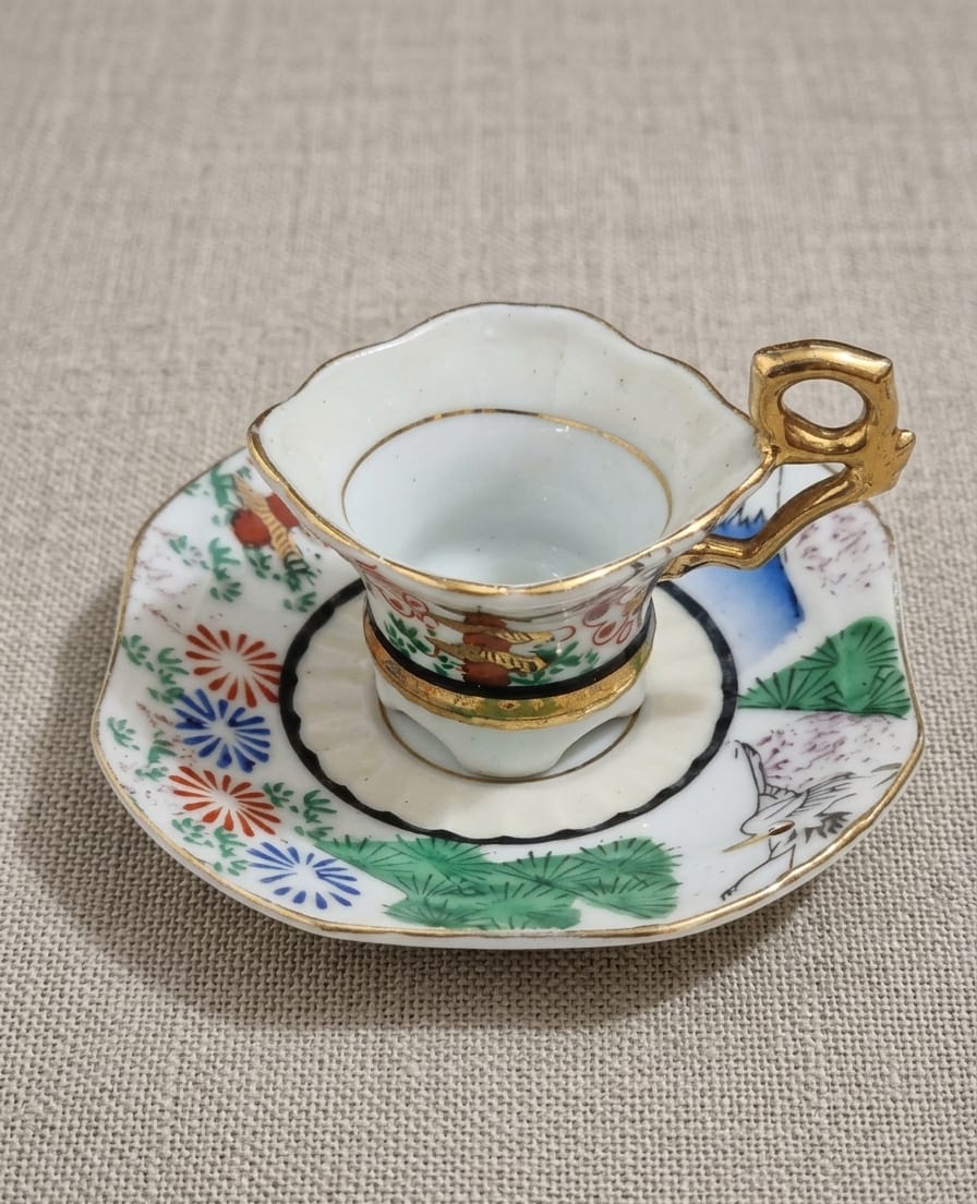 XÍCARA E PIRES EM MINIATURA,  DITA "UM GOLE" EM PORCELANA COM DECORAÇÃO ORIENTAL. MEDIDA DO PIRES 8CM.  MEDIDA DA XÍCARA 4,5CM DE DIÂMETRO E 3,5CM DE ALTURA.