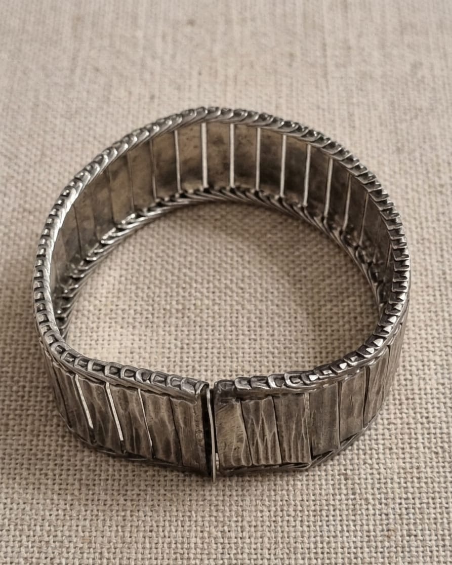 PULSEIRA EM METAL PRATEADO, MEDINDO 19CM ABERTA E 2CM DE LARGURA.