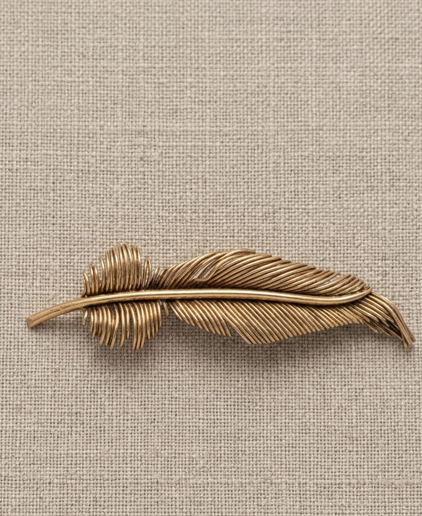 ANTIGO BROCHE PRODUZIDO EM METAL DOURADO, REPRESENTANDO PENA. MEDIDA 9,5CM. MARCAS DO TEMPO CONDIZENTES COM A IDADE.