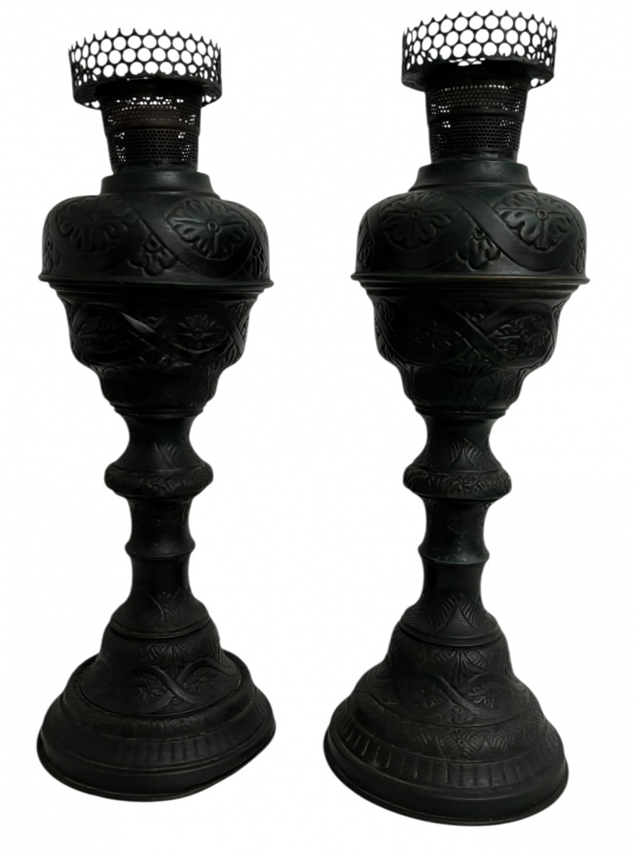 Par de antigas luminárias de mesa em metal patinado de tonalidade escura, ricamente trabalhados em relevo com motivos florais e arabescos. Peças de corpo torneado, base circular e bocal vazado com galeria perfurada, ...