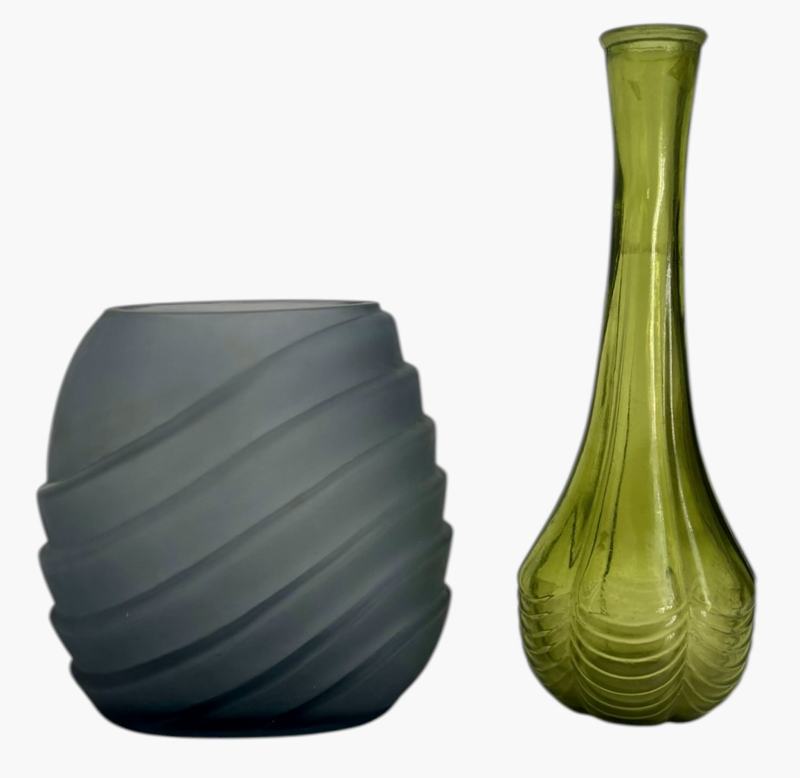 Conjunto com dois objetos decorativos em vidro artístico: vaso solitário em vidro verde translúcido, corpo alongado e base ondulada; e recipiente/castiçal em vidro fumê fosco, formato arredondado com sulcos em espiral. ...