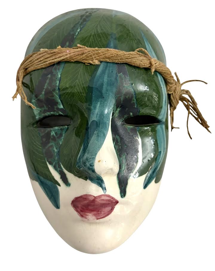 Máscara decorativa de parede, em porcelana esmaltada, representando face feminina estilizada, com pintura policromada em tons de verde, azul e lábios em vermelho. Peça com acabamento vitrificado e cordão lateral para ...