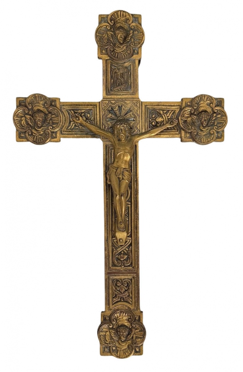 Importante cruz processional de parede em metal dourado, ricamente ornamentada com relevos em estilo neogótico, apresentando figura de Cristo crucificado e terminações com cabeças de querubins alados. Verso com argola ...