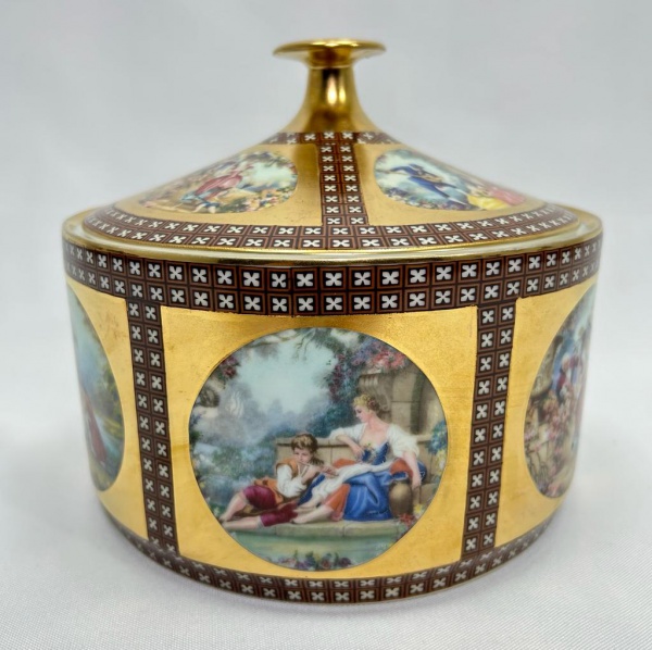 DP - PORCELANA - Biscoiteira confeccionada em porcelana manufatura DP, modelo Luis XV com policromia feita à mão com motivos de cena galante europeia realçada com fundo dourado e cruzetas. Medidas: 19,5x17 cm.