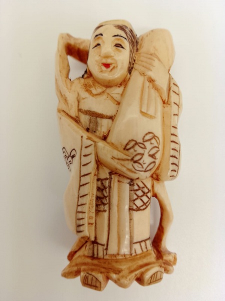 MARFIM / JAPÃO  ( Era Meiji - 1868/1912) - Netsuke, de coleção, confeccionado em marfim japonês policromado finamente lavrado na representação de mulher carregando instrumento musical . Dimensão: 5 cm de altura.