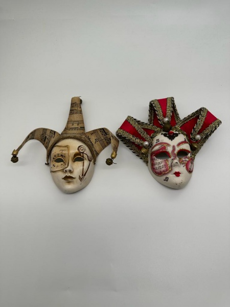 COLECIONISMO - Duas máscaras venezianas para adorno de parede, confeccionadas em faiança, pintadas à mão, ornamentadas com desenhos artesanais ricamente policromados, remetendo a notas musicais e chapéus. Medidas: maior: alt 21 cm/ menor: 18 cm, aproximadamente.