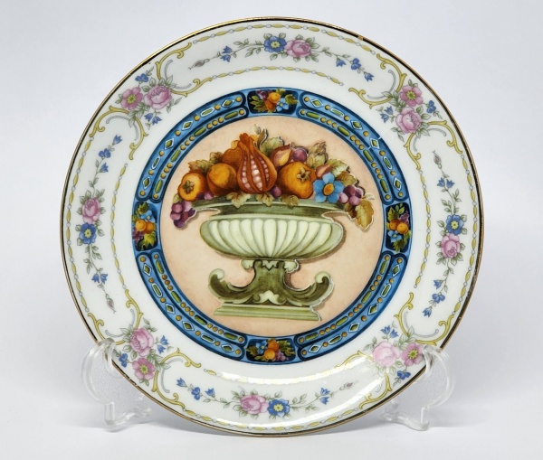Belíssimo prato decorativo em porcelana D&D com cena central de cesta de frutas, detalhes florais e filetado a ouro. Apresenta fio de cabelo. Diâmetro: