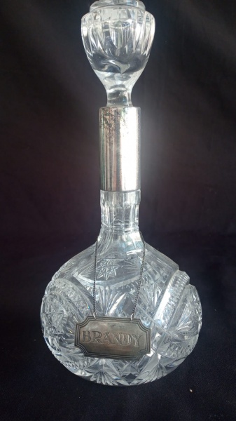 Antiga licoreira em cristal da boêmia em translúcido com gargalo revestido em prata e placa em prata gravado brand, teor 925. Medida  26cm x 11,5cm.
