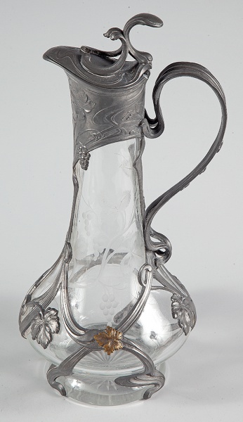 Art Nouveau - Jarra "decanter" de cristal lapidado com ramos de parreira e guarnição de metal prateado em feitio de ramos que entrelaçam seu corpo. Europa. 34 cm.