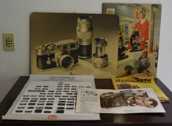 Dois antigos posters de propagandas da máquina fotográfica LEICA e de microscópios, poster da genealogia das máquinas `Leica`, ilustração com detalhamento de equipamento fotográfico e antiga revista `Shutterbug` (maior 58cm x 43cm)