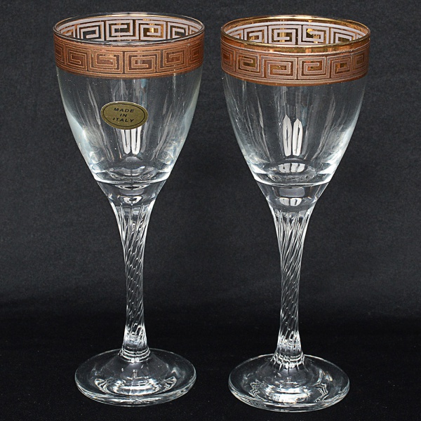 CRISTAL, par de taças para vinho confeccionadas em cristal italiano, haste torneada sobre base circular, bordas superiores decoradas com gregas em vasta douração. Medidas 19 x 7 cm