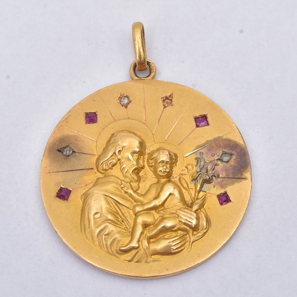 ARTE SACRA - Pingente redondo em ouro 18 k  representando São José e menino Jesus decorado por rubis (falta um). Medida: 2,8 cm. Peso: 6 gramas