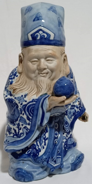 Gracioso mago chinês em porcelana com kimono em tons de azul e uma esfera apoiada em sua mão, marca