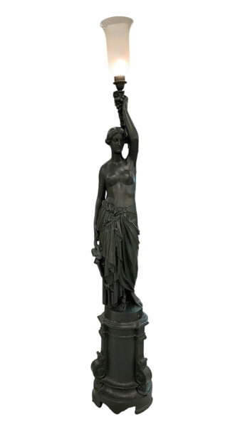 Imponente luminária de pedestal em ferro forjado representando figura feminina seminua segurando has