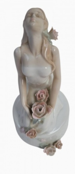 Encantadora escultura decorativa antiga (bibelô) executada em porcelana de excelente qualidade com acabamento esmaltado de alto brilho. A peça retrata uma esbelta e poética figura feminina ajoelhada com a cabeça alçada em expressão contemplativa e serena. Apresenta minucioso e delicado trabalho de aplicação artesanal de botões de rosas e folhagens modeladas em relevo policromado nos tons rosa pastel e verde, distribuídos na cabeça, no colo e ao longo da base. Paleta de cores suaves e estética romântica fortemente inspirada na renomada escola de porcelana espanhola. Uma peça clássica de excelente efeito estético e grande apelo para colecionadores de porcelanas artísticas finas.Dimensões: 20 cm de altura x 10 cm de diâmetro da base circular.
