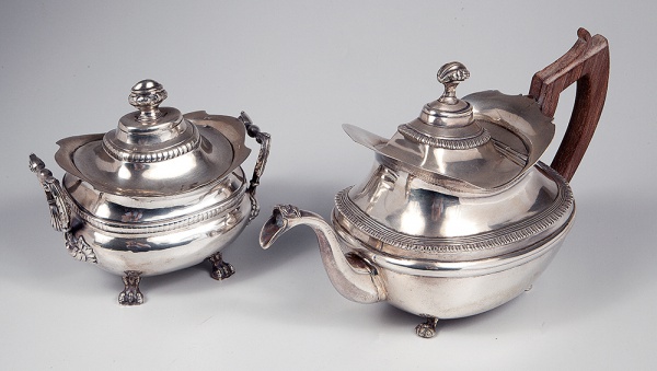 Conjunto de bule e açucareiro em prata de lei portuguesa com contraste da cidade do Porto. Maca de ourives com as iniciais ND (Moitinho P-539-0, não identificado, conhecida com a marca do ensaiador P-16.0. Executados com corpo bojudo com bordas alargadas e recortadas, tampas abobadadas com pegas repuxadas e cinzeladas com motivos florais. Bico levemente recurvado. Repousando sobre quatro pés zoomórficos elevados. Complementos com gomos e perolados segmentados ao redor do bojo e da tampa. Século XVIII/XIX. Maior possui 18 x 29 x 13 cm. Peso bruto: 1.768g.