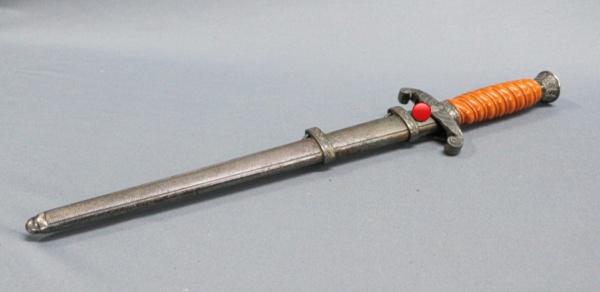 Punhal militar alemão Segunda Guerra com bainha metálica cabo em baquelite alaranjado com detalhe da águia nacional em metal guarda em arabescos lâmina em bom estado com sinais de desgaste no conjunto comprimento 36 cm - A Bastos Leilões não faz apologia a quaisquer movimentos políticos ou ideológicos, bem como repudia qualquer ideologia de cunho racista.