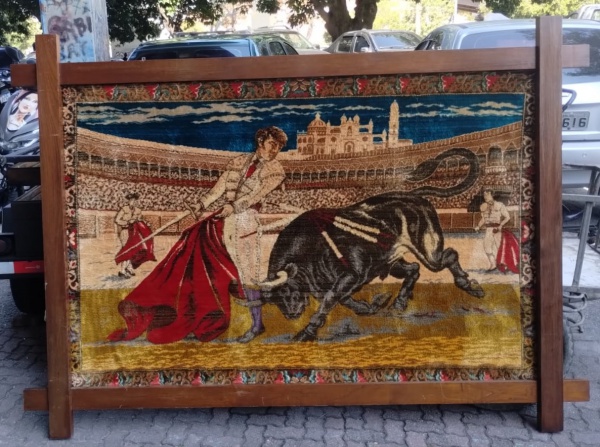 TAPEÇARIA - Lindissimo quadro em tapeçaria emoldurada em madeira nobre,  (A cena central apresenta um toureiro com a tradicional capa vermelha, confrontando com um touro preto em uma arena ), a tourada é uma tradição cultural, especialmente na Espanha e em Portugal, que envolve a luta entre toureiro e touro em uma arena, peça em cores que se destacam tapeçaria realmente muito bonita. medindo 208cm x148cm