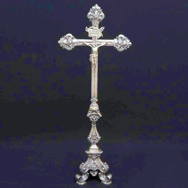 Magnífico <b>crucifixo </b>em prata brasileira do séc. XIX. Cruz em caneluras com três ponteiras lindamente trabalhadas em "rocailles" barrocos. Haste movimentada decorada com folhas de acanto sobre base trípode de aba gomada e decoração em harmonia ao conjunto. Contraste 10 Dinheiros e marca do ourives dso Rio de Janeiro Domingos Farini, citado entre 1848 e 1883, conhecida com marcas do toque BR-156.0 e BR-162.0. Alt. 89 cm