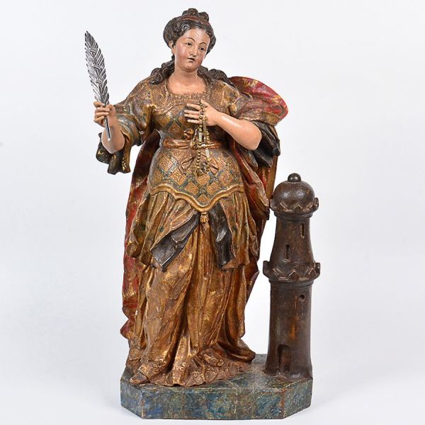 Belíssima imagem de <b>Santa Bárbara </b>de lindas e plácidas feições, em madeira entalhada, com vestes sobrepostas destacando o gracioso corpete com saiote plissado. Suntuosa policromia realçada com volutas a ouro. Nota-se o elaborado tratamento dado aos cabelos. Ao lado esquerdo a torre de três janelas e à mão direita, a palma do martírio em prata. Acompanha um terço. Séc. XVIII. Alt. 73 cm