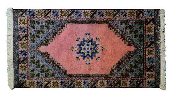 Marrocos.  Tradicional tapete Rabat de produção manual. Trama de algodão e urdidura em lâ. 73 x 145 cm, com as franjas. Em perfeito estado de conservação. Leia mais: Os tapetes Rabat são a joia da coroa do artesanato têxtil marroquino. Apesar de derivarem seu nome genérico da cidade que é capital do país desde 1912, podem ser feitos em outros centros produtores - como Casablanca, Fez e mesmo em Marrakech. Certa lenda narra, fantasiosamente, que, no século 17, um pássaro trouxera no bico, deixando-o cair no pátio aberto do palácio do sultão, um pedaço de tapete da Anatólia otomana, e que daí derivariam os tapetes Rabat. Na verdade, trata-se de uma leitura citadina de desenhos tradicionais berberes: o motivo do losango é chamado riad (jardim, em árabe); o medalhão central sendo um estanque de água - como ocorre nos velhos palácios magrebinos. Os demais desenhos podem ser o da borboleta (símbolo de Maomé), a chaleira (representa a hospitalidade), a mão de Fátima (os cinco pilares do Islã), estrelas, animais, signos mágicos berberes... Feitos de lã sobre lã ou de lã sobre algodão (caso desta peça), os Rabat  superiores podem ser exportados com a estampilha de qualidade do Reino do Marrocos.