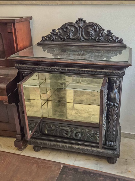 Antigo Móvel Bar, em madeira nobre, com entalhes ornamentados com figuras femininas, conhecidas como  Cariátides, e fitomórficas, com características que remetem ao estilo manuelino e Renacentista, com interior espelhado e prateleiras em vidro para armazenar Bebidas e Taças. No tampo apresenta um alçado, que completa o estilo clássico. Dimensões: 140 cm X 105 cm X  56 cm (Alt./Larg./Prof.). Espelho com manchas do tempo. RETIRADA COM AGENDAMENTO PRÉVIO POR CONTA DO ADQUIRENTE OU TRANSPORTADORA INDICADA, EM CASA TÉRREA DA LAPA, RIO DE JANEIRO/RJ, IMPRETERIVELMENTE ATÉ O DIA 18.11, DATA DA ENTREGA DAS CHAVES DO IMÓVEL VENDIDO.                                                                                                              Cariátides são esculturas femininas, usadas como colunas ou pilares arquitetônico, na antiga cidade grega de Cária, onde as mulheres eram conhecisas pela sua beleza e força. Foram usadas pela primeira vez na arquitetura grega clássica, cujo exemplo mais famoso são as cariátides do Erecteion, na Acrópole de Atenas. O uso de cariátides foi retomado posteriormente, como no movimento Renascentista, tornando-se populares em móveirs de decoração.