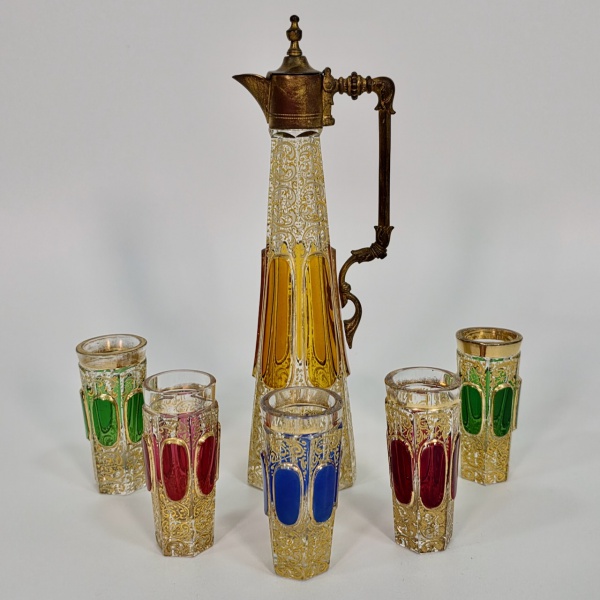 Raro licoreiro da Bohêmia em cristal overlay amarelo no caso da garrafa e copos em overlay verde, azul e vermelho,  com farta decoração a ouro em alto relevo, composto de garrafa e cinco copos, peça de alta cotação internacional, alt. da garrafa 22 cm e dos copos 7 cm, o copo azul com mínimo bicado na borda, vide foto adicional.
