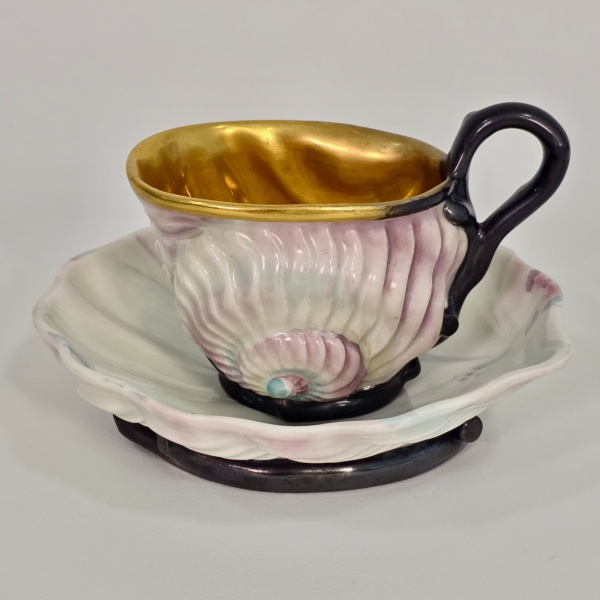 Vienna Imperial - Raríssima xícara e seu pires em porcelana Imperial de Viena na forma de caracol e amêijoa respectivamente, circa 1826, estilo Biedermeier, pintada por Josef Geyer, de um formato muito especial, com aparência naturalista, xícara com farto ouro em sua parte interna, ambas as peças em porcelana branca parcialmente pintadas em tons de violeta, cinza e turquesa marcadas e numeradas no fundo; pires com 15 x 14,5 cm e alt. 3,5 cm, xícara com 12 x 8 cm inclusa a alça e alt. 9 cm, mínimo desgaste no ouro do interior da xícara. Uma xícara e seu pires de mesma forma mas com pintura diferente foram exibidos no Castelo de Liechtenstein, em Viena, em 1910, vide foto adicional. Peça de alta cotação internacional, localizamos apenas um exemplar similar vendido por 1800 Euros, vide  foto adicional com print do site.