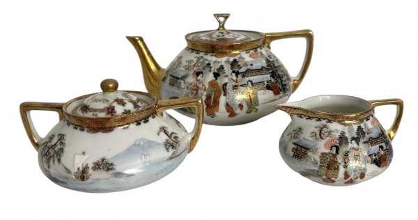 SATSUMA JAPÃO  Conjunto de porcelana Satsuma composto de três peças finas em porcelana japonesa pintadas à mão com cenas de gueixas e paisagens, detalhes em douração e alças geométricas em ouro. Composto por bule, leiteira e açucareiro com tampas.Marca em vermelho sob a base.Peças em ótimo estado, com mínima perda de dourado pelo tempo. Medida do maior 19cm.