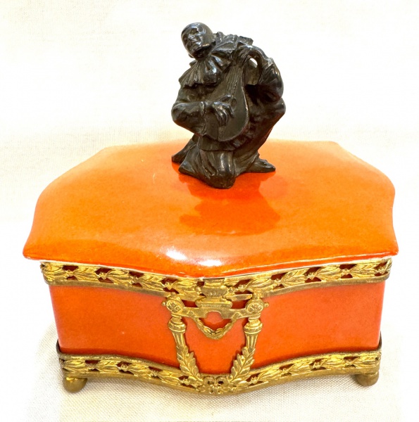 Germany circa 1920 - Elegante e Antigo Porta Joias em porcelana Alemã na cor coral com detalhes em bronze e pega da tampa com figuras de Arlequim, peçamarcada. Med. 13 X 14X 10 cm.