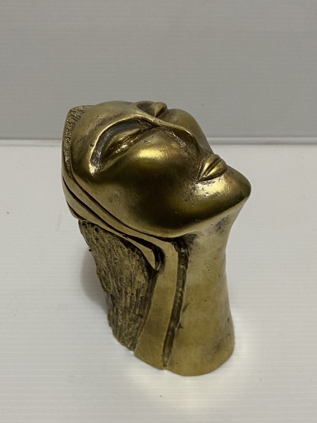 Estatueta de bronze retratando rosto feminino olhando para cima, envolto em um material que se mescla à base texturizada. Dimensões: 12 cm.