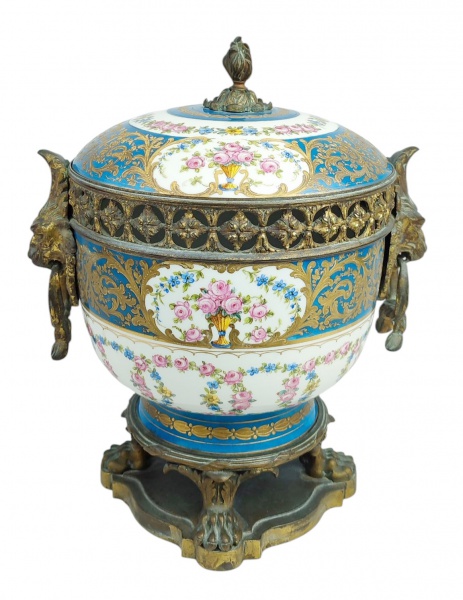 Sèvres - Antigo e grande potiche para aromatizantes em bronze e porcelana francesa, com marca da manufatura, decorado com pintura floral policromada e ricos detalhes em dourado. Alças no formato de cabeça de leão. Pés em pata. Bronze com desgastes causados pelo tempo. Med. 35,5x30x24cm.