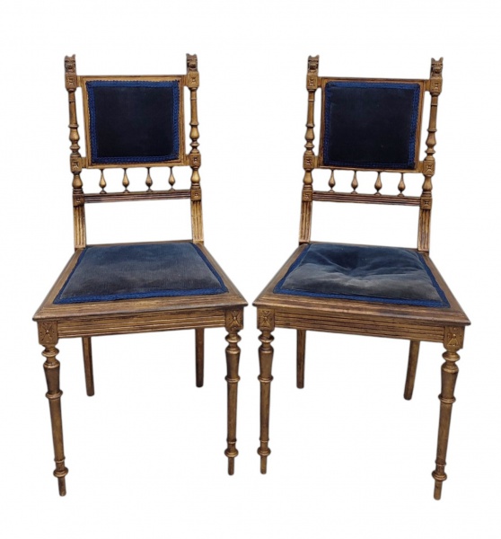 Par de cadeiras em madeira patinadas de dourado e entalhadas em flores e sobre os encostos cabeças de leão, sendo estes e os assentos estofados e forrados com tecido azul. Uma com fissura em uma trava do encosto e a outra com colagens no encosto. Med. 91x44x40cm.