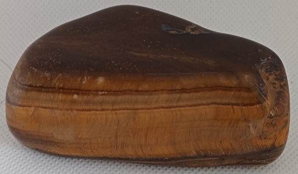 OLHO DE TIGRE, ROLADA JUMBO - Pedra rolada jumbo é uma pedra natural que passou por um processo de rolamento para adquirir uma forma arredondada e polida, e que se caracteriza por um tamanho maior, geralmente superior a 4cm. Essas pedras são frequentemente utilizadas em decoração, terapias e como peças de coleção, devido à sua beleza natural e versatilidade. O olho de tigre promove Proteção e Prosperidade. Aproximadamente 195 g - 8 x 4 x 3 cm.