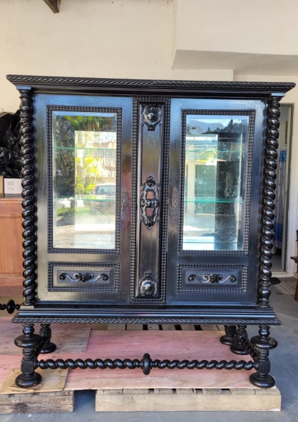 Cristaleira antiga em madeira nobre de lei, no estilo Manuelino (também conhecido como gótico português tardio), caracterizada por seu design rebuscado e histórico, com colunas torneadas em espiral, lindos entalhes detalhados em relevo, duas prateleiras de vidro e portas lateral e fundo em vidro, med. 1,40m largura x 0,53cm profundidade x 1,60m altura