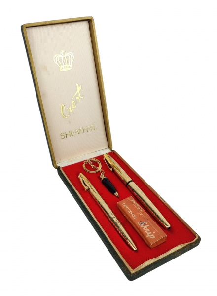 Conjunto de 3 canetas americanas, com marca da manufatura Sheaffer, sendo 2 em metal dourado (uma bico de pena e outra esferográfica) e a outra em baquelite, esferográfica, com argola e corrente para chaveiro. Na caixa. Necessitam recarga. As maiores apresentam gravado as iniciais e o nome "La Es. E. F. E. Jbo. Maj. Nilo. Comp. da maior 14,5cm.