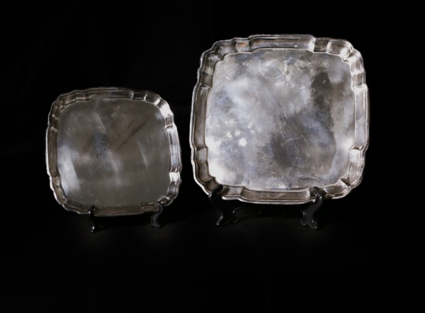 SHEFFIELD PLATE - Conjunto de duas bandejas quadradas com cantos suavemente recortados e moldura em relevo, de estilo inglês clássico. Produzidas no padrão Sheffield Plate, com acabamento prateado e design tradicional. Peças elegantes, ideais tanto para serviço quanto para composição decorativa sobre aparadores ou mesas. Apresenta marcas de uso. Medidas: 28 cm x 28 cm (maior) e 21 cm x 21 cm (menor)