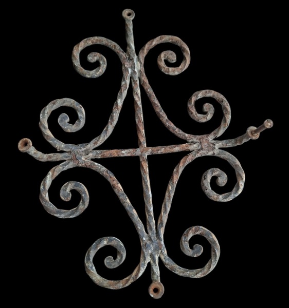 Antiga grade decorativo de ferro forjado, para janela de porta com um design simétrico em forma de cruz adornada com volutas (espirais) nas extremidades. Parece ser uma peça de artesanato antigo ou um