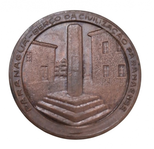 Medalha de bronze anverso com desenho central de tronco de castigo de escravo com prédios ao redor com a inscrição na borda " Paranaguá berço da civilização paranaense" no verso no centro brasão com c