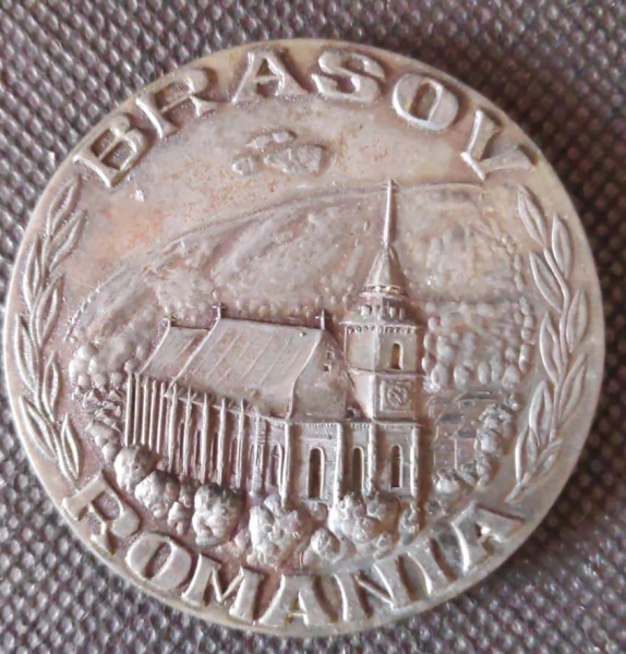 Medalha com imagem de igreja da parte central em relevo com as palavras Brasov Romania nas bordas na parte posterior figura de prédio em relevo com as mesmas palavras nas bordas. Diam. 60mm