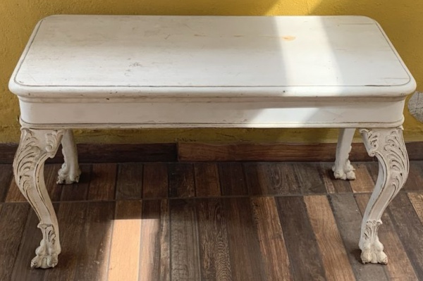 Antiga mesa de madeira nobre laqueada de branco, apresentando ínfimas rachaduras no tampo, pés torneado no formato pata de Leão, formato arqueado com entalhes em Ramos. Med. 45cm x 90 cm x 51cm