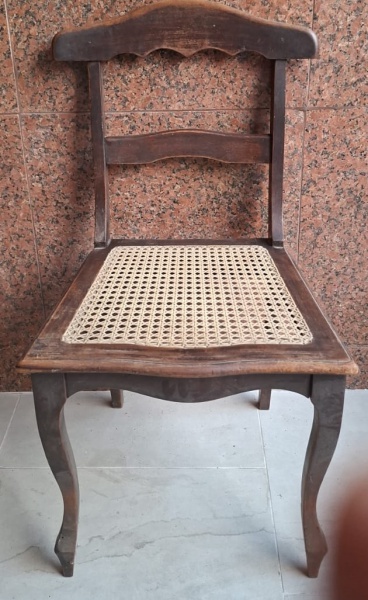 Cadeira de madeira com um assento trançado (vime ou rattan), estilo vintage, com pernas curvas e um encosto simples de duas barras horizontais. Parece ser um modelo clássico de cadeira de madeira com