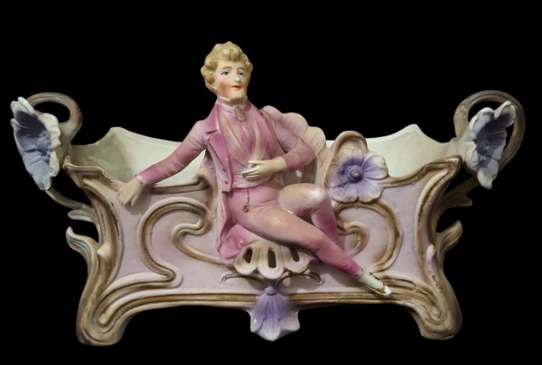 Jardineira/centro de mesa porcelana biscoito policromada - 9x14x26,5cm - Peça estilo Art Nouveau/Belle Époque. Figura masculina sentada na jardineira com flores nas alças. Muito comum Europa anos 1900