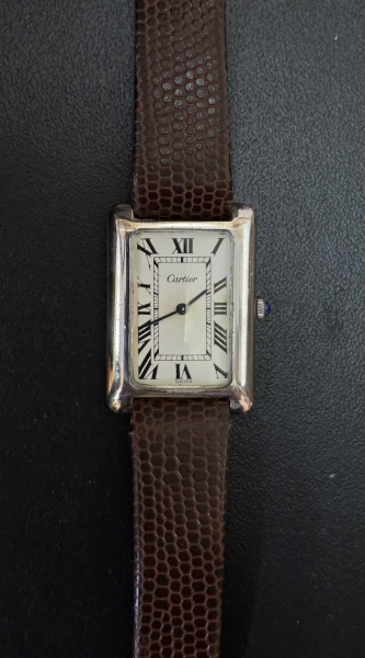 CARTIER TANK - Relógio suíço de pulso. Caixa em aço, visor em acrílico. Mostrador branco com alagarismos romanos em preto. Movimento a corda. Pulseira em couro marron, não original com fivela original