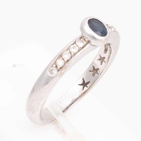 Anel em ouro branco, contrastado 750 K, cravejado com dez brilhantes de aproximadamente 3 pontos cada e uma safira azul. Aro 17. Peso 4,8 gr. (Por medida de segurança esse lote não se encontra em noss