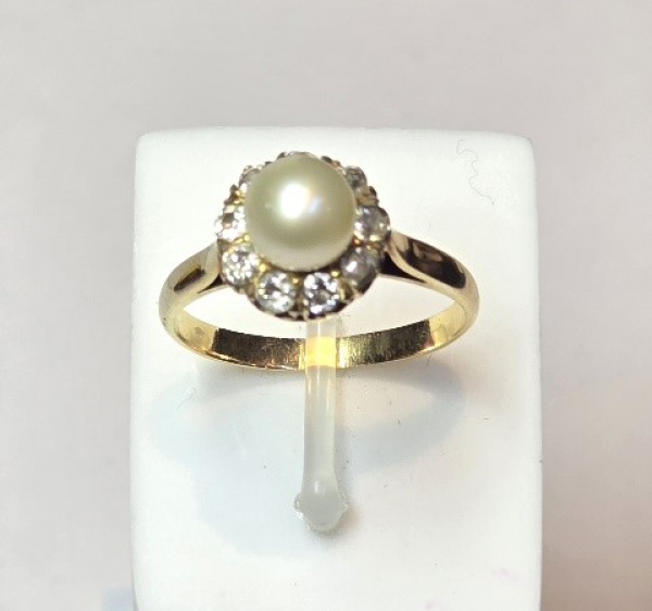 Anel em ouro amarelo 18 k, com pérola central de aproximadamente 6 mm rodeada de diamantes. Aro 15. Peso 2,9 gr. (Por medida de segurança esse lote não se encontra em nossa loja).